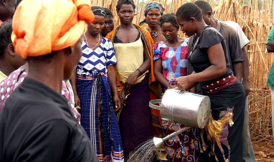 Eine Gruppe von Menschen ist um Annie versammelt. Annie hält eine Gießkanne