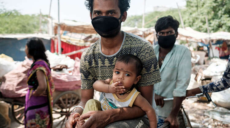 2020-coronavirus-slum-ranjeet-kumar-delhi-indien-c-florian-lang.jpg Ein Mann mit Mundschutz, er hält ein Baby auf dem Arm.