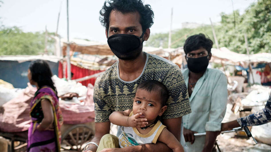 Ein Mann mit Mundschutz, er hält ein Baby auf dem Arm.
