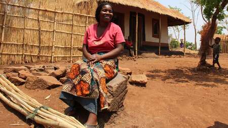 Frau sitzt vor Hütte auf einem Hocker