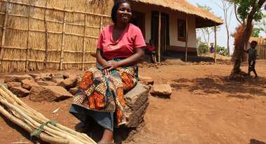 Frau sitzt vor Hütte auf einem Hocker