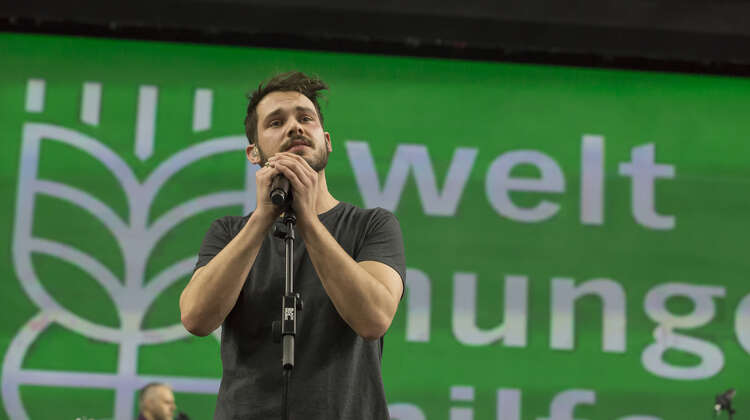 Robert Redweik auf der Bühne, im Hintergrund das Welthungerhile-Logo.