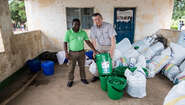 Zwei Männer, einer davon trägt ein grünes Welthungerhilfe-T-Shitrt, stehen vor großen Säcken voller Hilfsgüter.