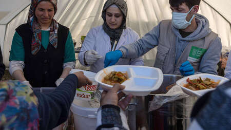 Zwei Frauen und ein Mann stehen in einem Zelt und verteilen Mahlzeiten.