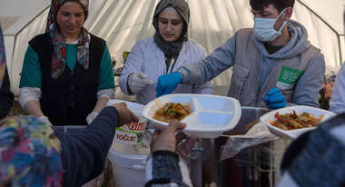Zwei Frauen und ein Mann stehen in einem Zelt und verteilen Mahlzeiten.