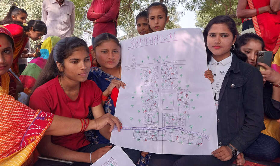Eine Gruppe junger Menschen in Indien hält ein großes Blatt Papier mit einer Kartierung ihres Dorfes