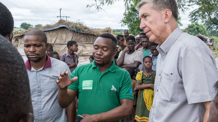Eine Gruppe von Männern im Gespräch. Im Hintergrund viele Kinder, Frauen und Männer.