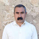 Ein Mann steht an einer Wand und schaut in die Kamera.