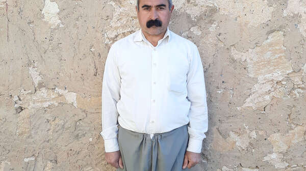 Ein Mann steht an einer Wand und schaut in die Kamera.