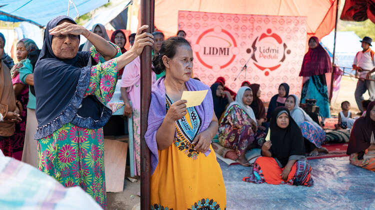 2019-nothilfe-tsunami-ueberlebende-fluechtlingscamp_C_acted.jpg Frauen sitzen und stehen unter einem Zelt.