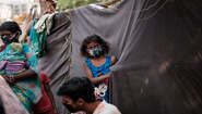 2020-coronavirus-maedchen-slum-delhi-indien-c-florian-lang.jpg Ein Mädchen mit Mundschutz steht an einem Zelt aus schwarzen Planen.