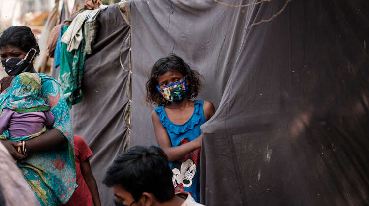 2020-coronavirus-maedchen-slum-delhi-indien-c-florian-lang.jpg Ein Mädchen mit Mundschutz steht an einem Zelt aus schwarzen Planen.