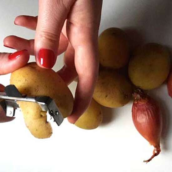 Nahaufnahme von Händen die Kartoffen und Zwiebeln schneiden.