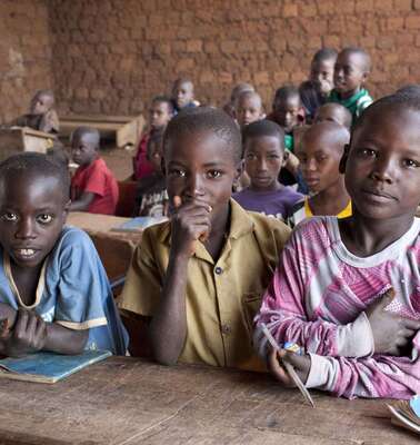 Drei Jungen sitzen im Vordergrund einer Schulklasse in Burundi