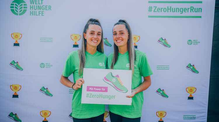 Die beiden Influencer-Schwestern "Leso Twins" tragen ein Schild mit der Aufschrift: "Mit Power für #ZeroHunger.