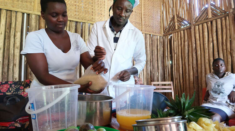 Eine Frau fügt Zucker in einen Topf. Daneben steht ein Mann in Kochkleidung