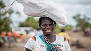 2019-zyklon-idai-hilfsgueterverteilung-nhamatanda-mosambik-tommy-trenchard-concern.jpg Eine Frau trägt ein Hilfsgüter-Paket auf dem Kopf und lächelt in die Kamera.