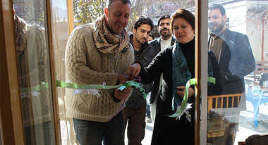 Welthungerhilfe-Mitarbeiter schneiden eine Scherpe vor einem Eingang feierlich durch.