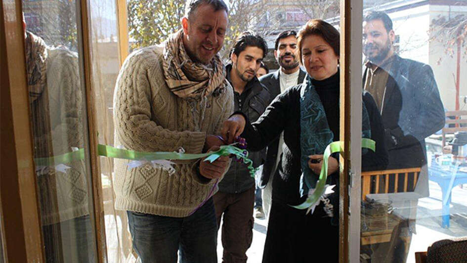 Welthungerhilfe-Mitarbeiter schneiden eine Scherpe vor einem Eingang feierlich durch.