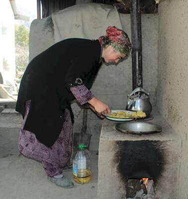 Eine Frau beugt sich mit einem Teller über einen niedrigen gemauerten Herd.