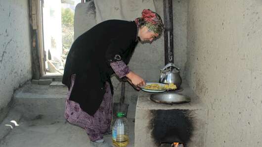 Eine Frau beugt sich mit einem Teller über einen niedrigen gemauerten Herd.