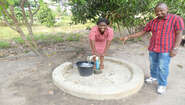 2021-sierra-leone-wasap-social-business-hand-drilled-well.jpg Eine Frau und ein Mann stehen an einer Wasserpumpe, Sierra Leone 2021.