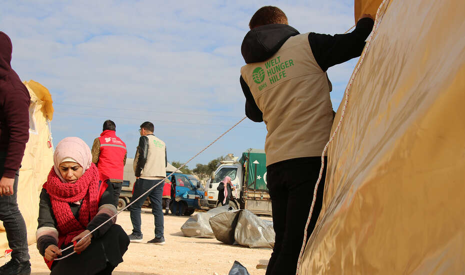 Zwei Menschen bauen ein Zelt als Notunterkunft auf.