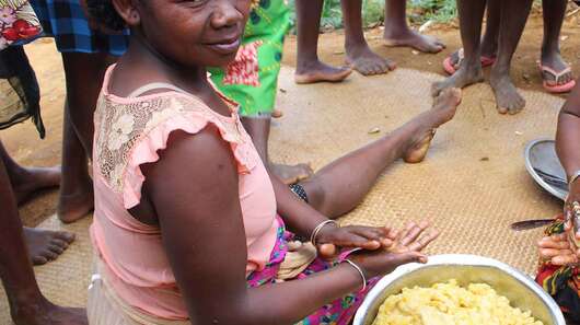 Zwei Frauen sitzen mit einer Schüssel voller Teig auf dem Boden und bereiten Essen zu.