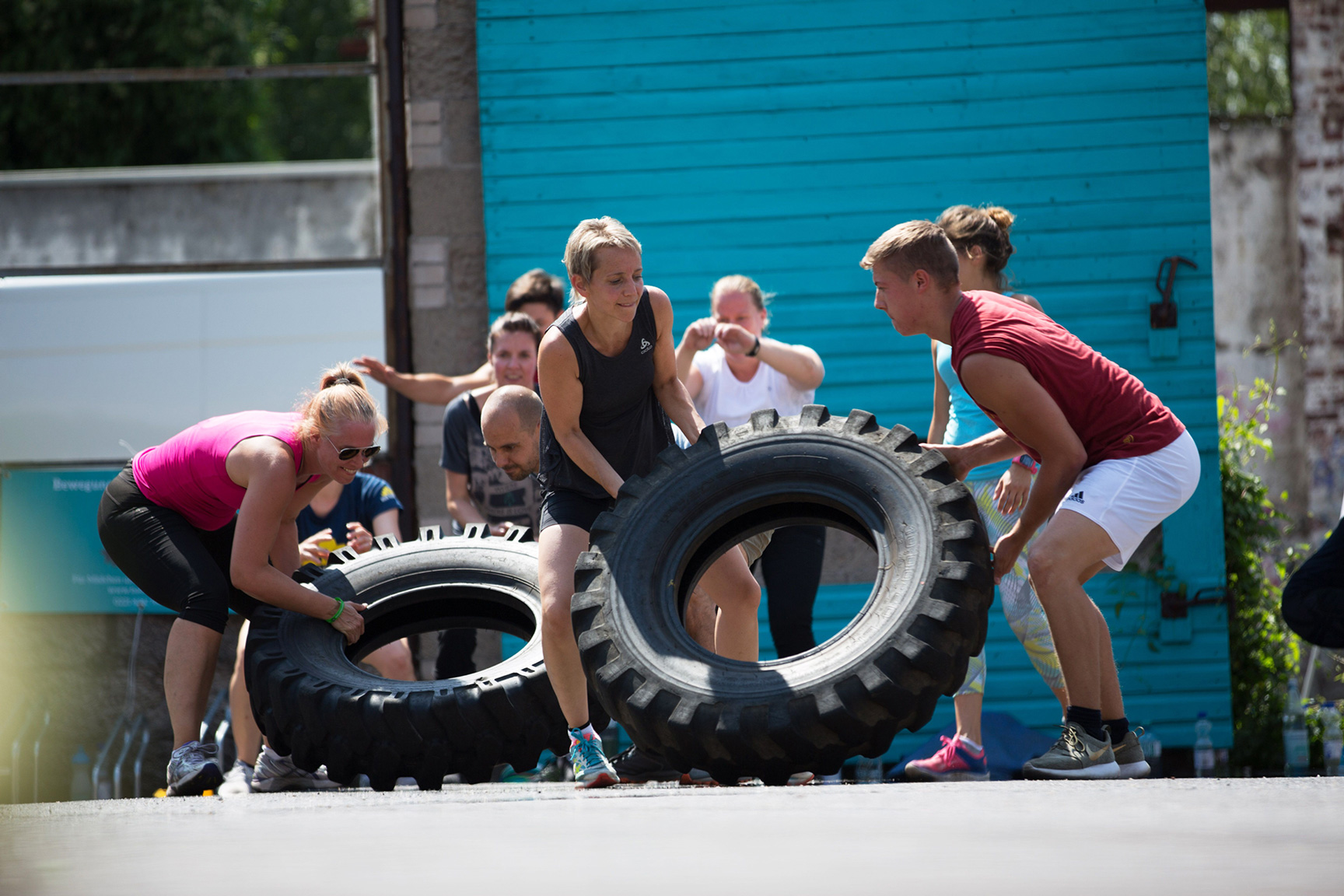 Menschen in Sportklamotten rollen große Reifen.