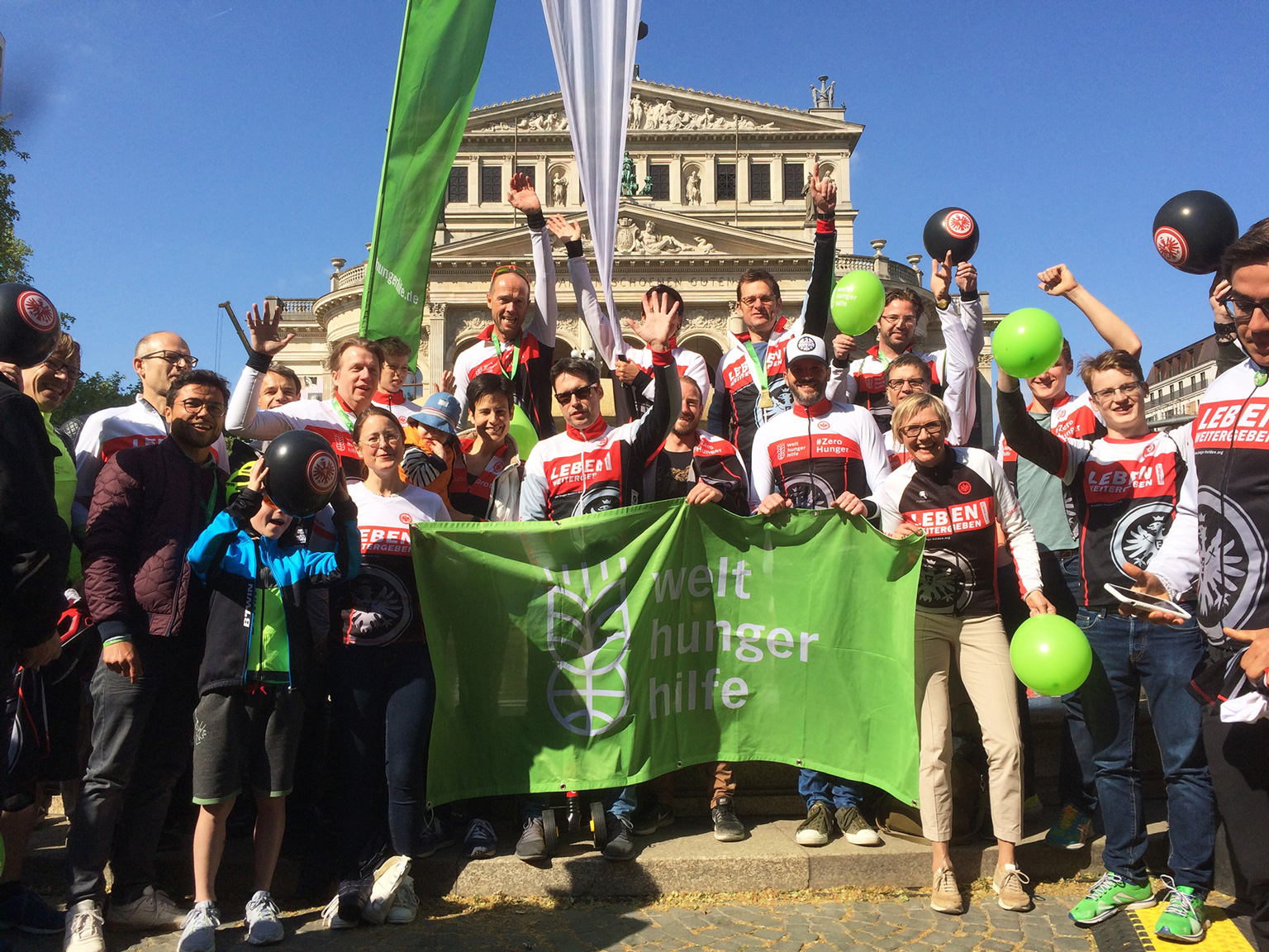 Eine Gruppe von Menschen mit Welthungerhilfe-Flagge schaut lachend in die Kamera.