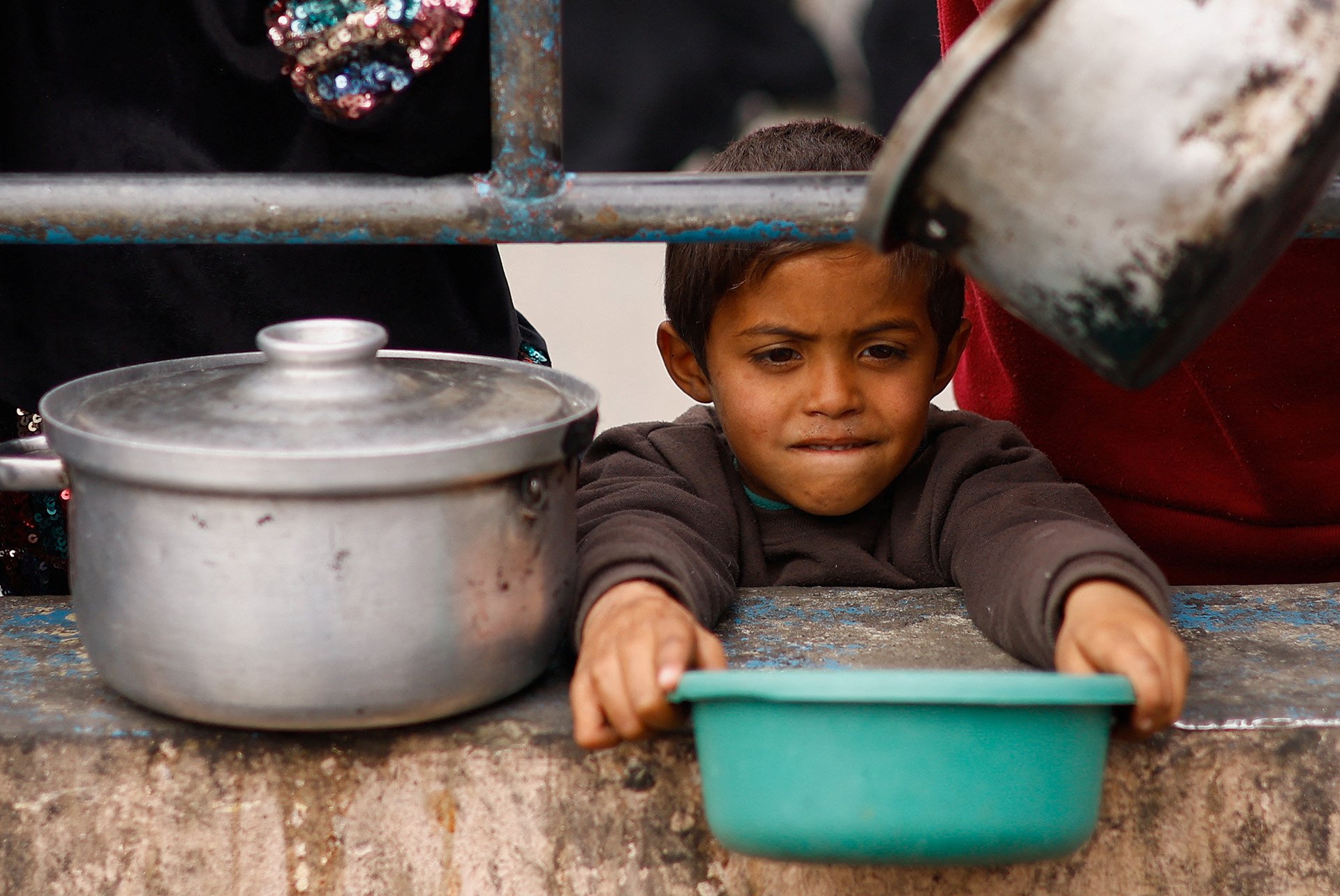 Ein kleines Kind hält eine Schüssel mit ausgestreckten Armen und wartet auf die Verteilung von Essen