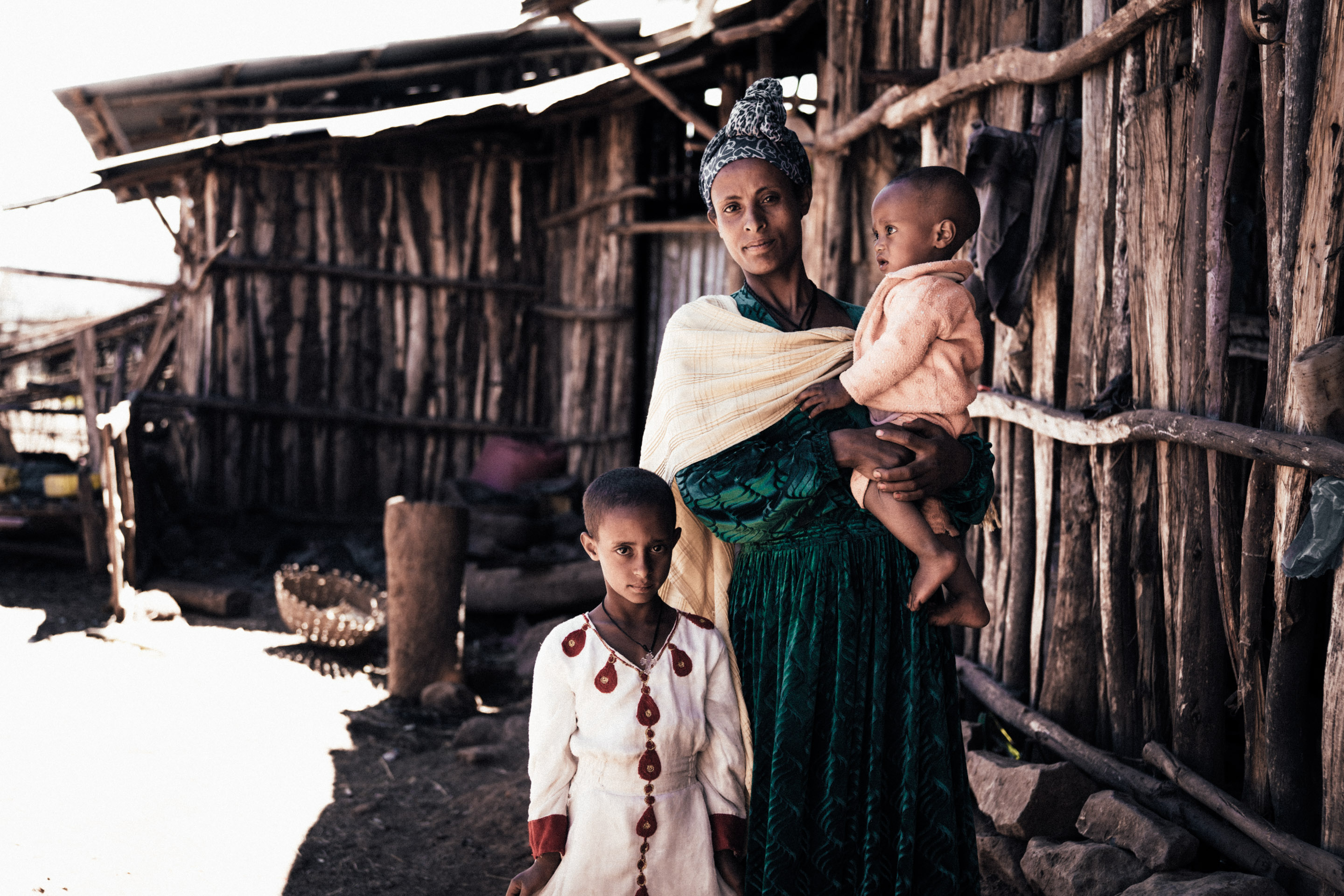 Eine Frau steht mit ihren beiden Kindern vor einer Holzhütte, Äthiopien.