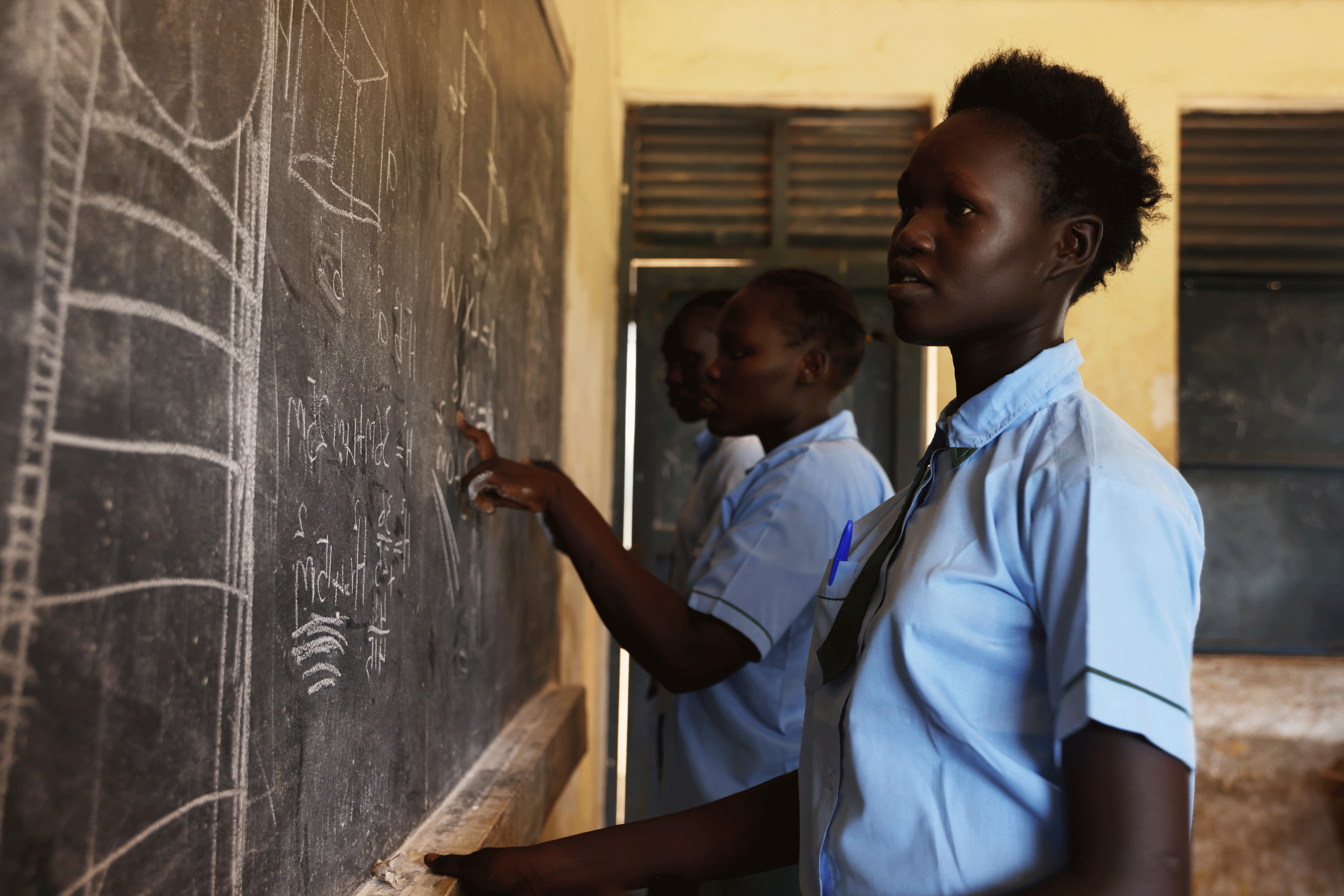 Bild aus einem Projekt im Südsudan mit Schulspeisungen, ein Mädchen steht an einer Schultafel.