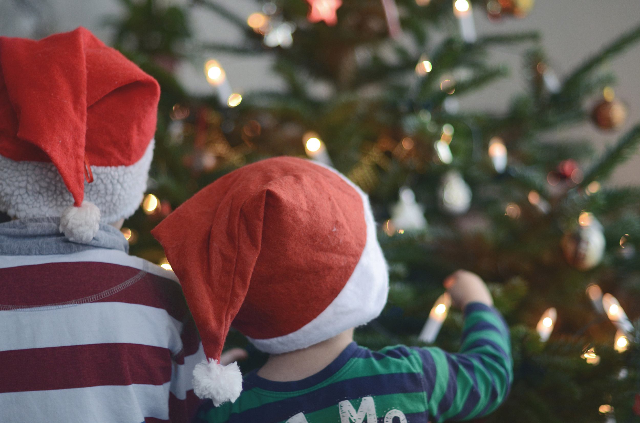 Anlassspende zu Weihnachten: Zwei Kinder mit Weihnachtsmützen vor dem Tannenbaum