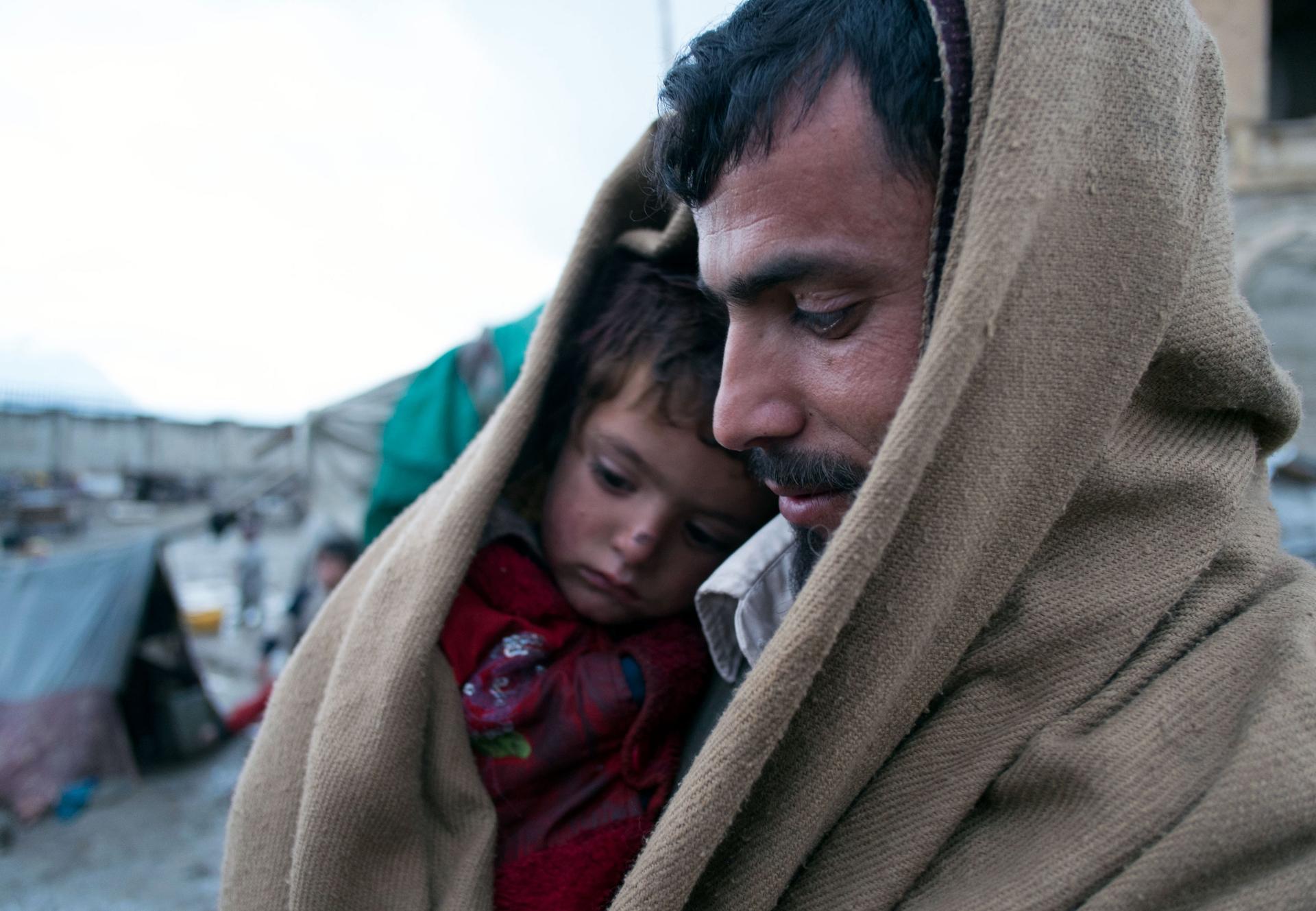 Vater sitzt mit Sohn zusammen in Decke eingehüllt im Flüchtlingscamp.