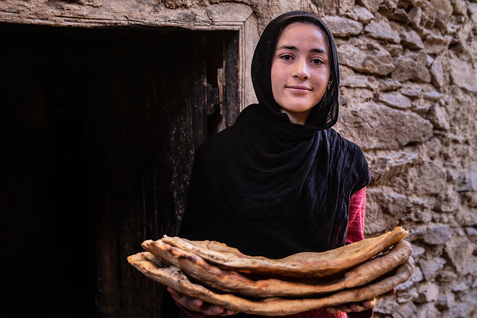 Eine Frau hält Fladenbrot und lächelt in die Kamera.