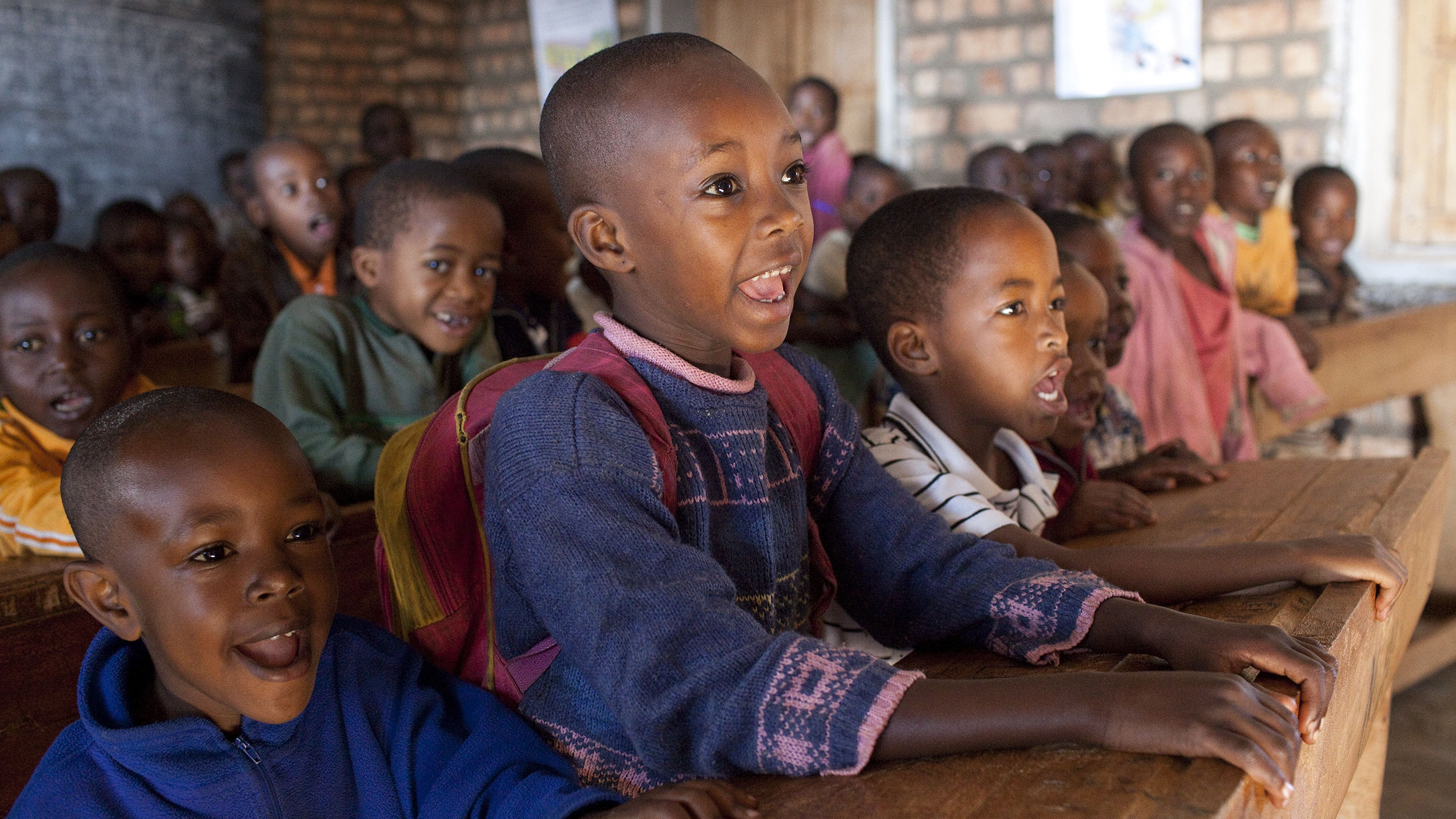Fröhliche Kinder sitzen auf Schulbänken und schauen Richtung Tafel