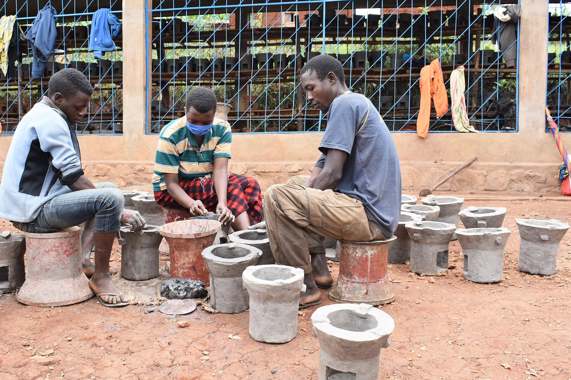 Drei junge Menschen sitzen sich gegenüber und töpfern Öfen, Burundi 2021 