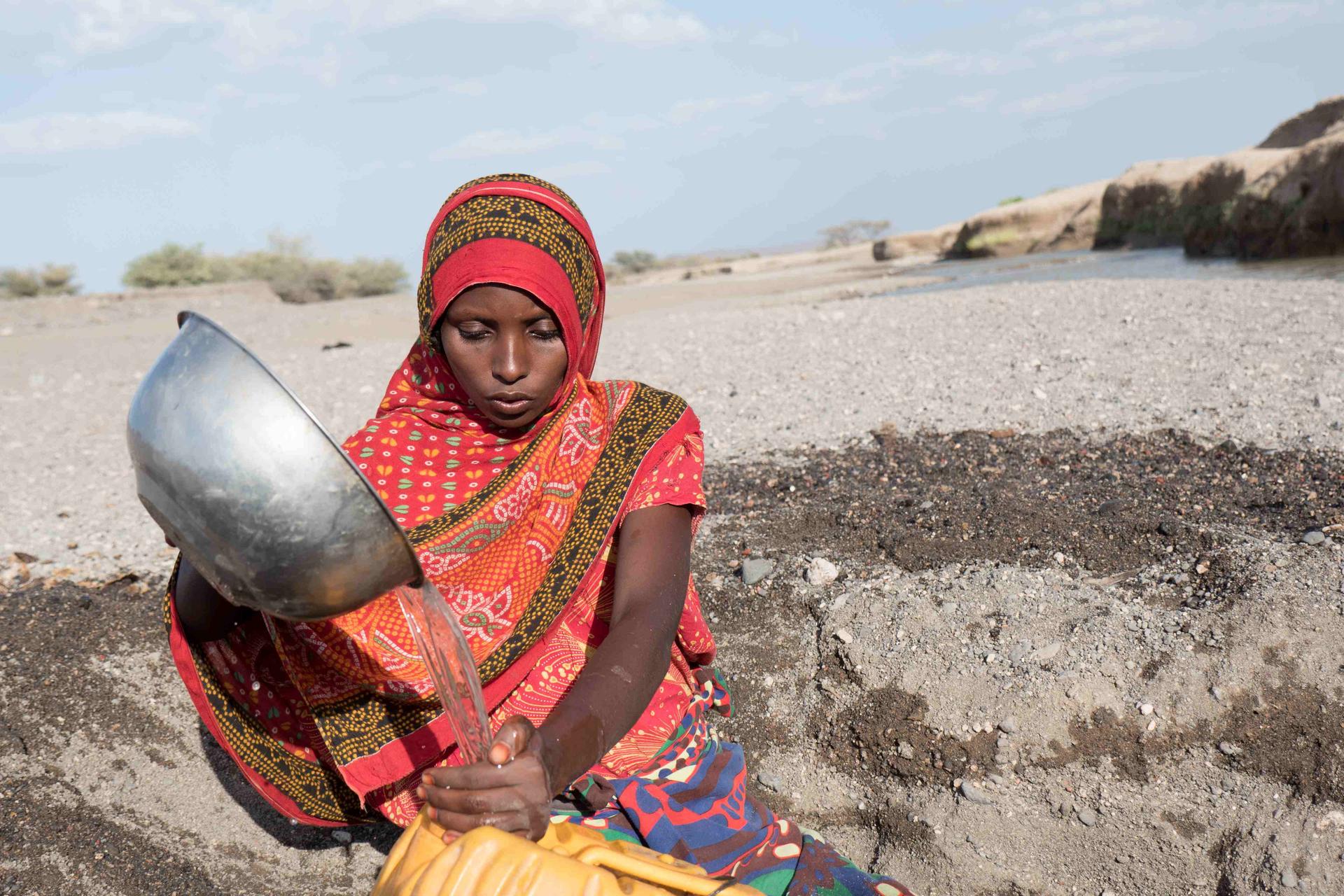 Eine Frau füllt in der Wüste Wasser aus einer Schüssel in einen Wasserkanister.