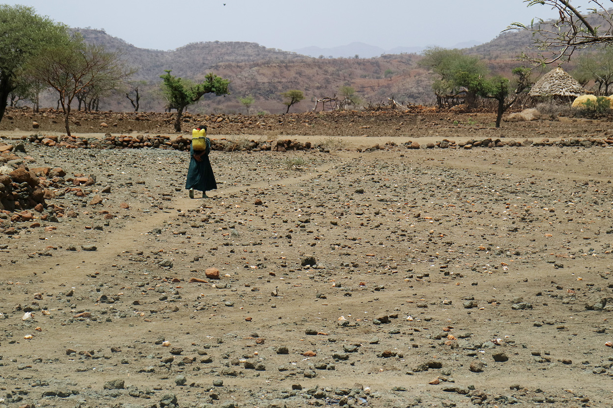 Ein Kind holt Wasser mit einem Kanister und geht durch eine ausgetrocknete Landschaft.