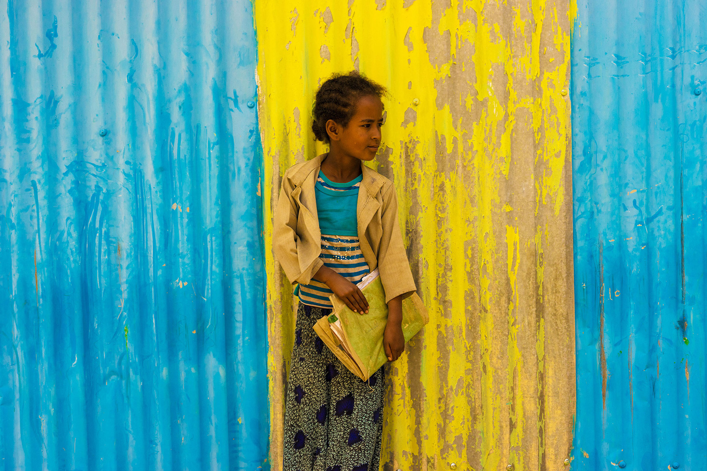Mädchen mit Schulmappe vor blau-gelber Wand