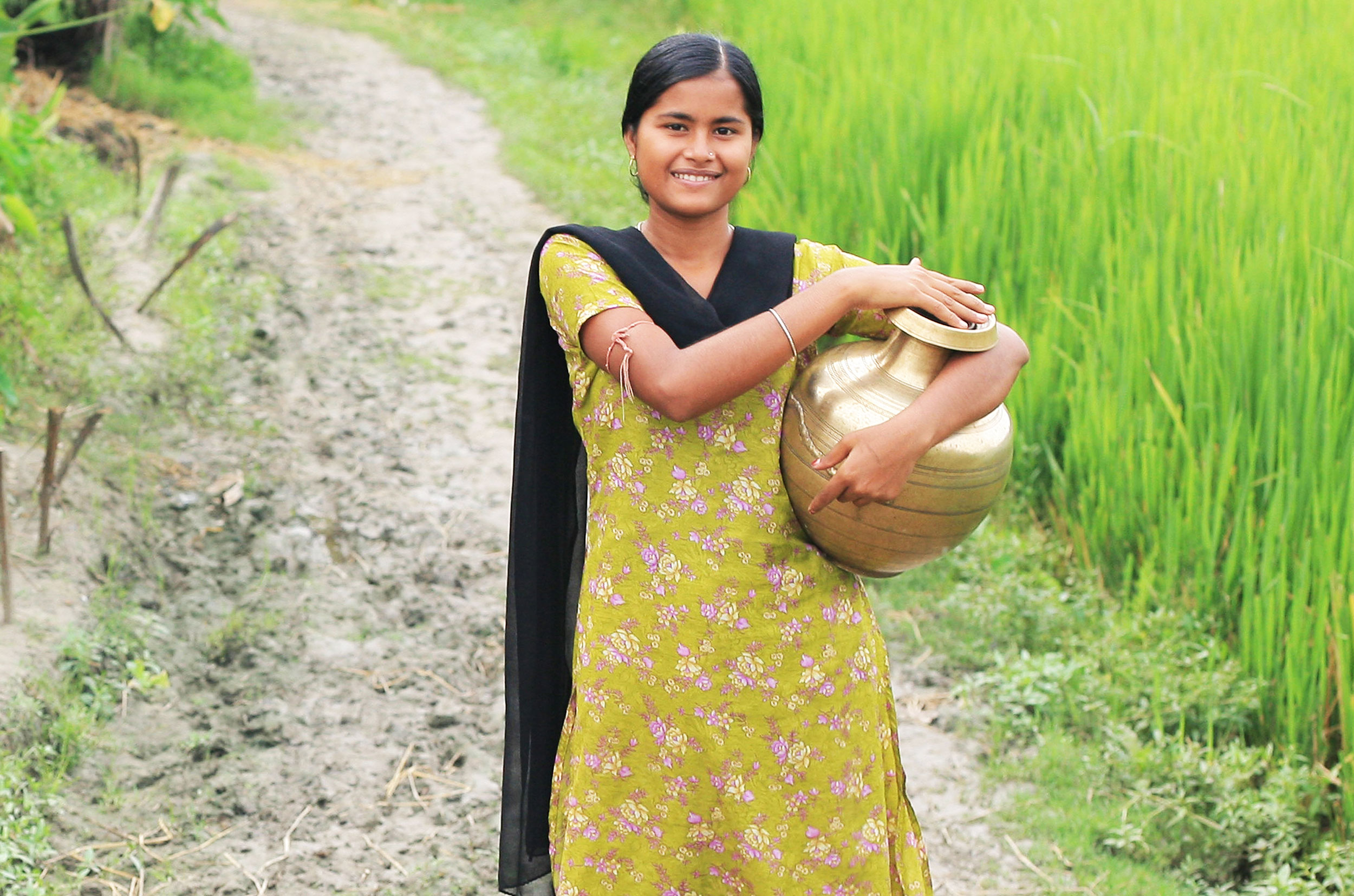 Frau im gelben Sari mit Wasserkrug unter dem Arm