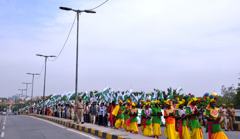 Indigene Demonstranten stehen in tarditionseller Kleidung und mit wehenden Fahnen am Straßrand.