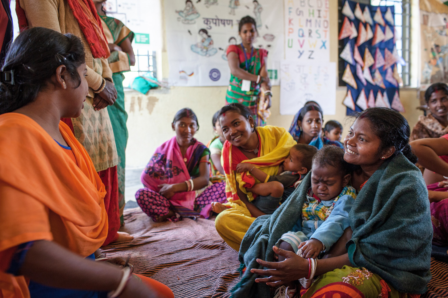 Frauen sitzen im Kreis und unterhalten sich. Manche haben Kinder auf dem Schoß.