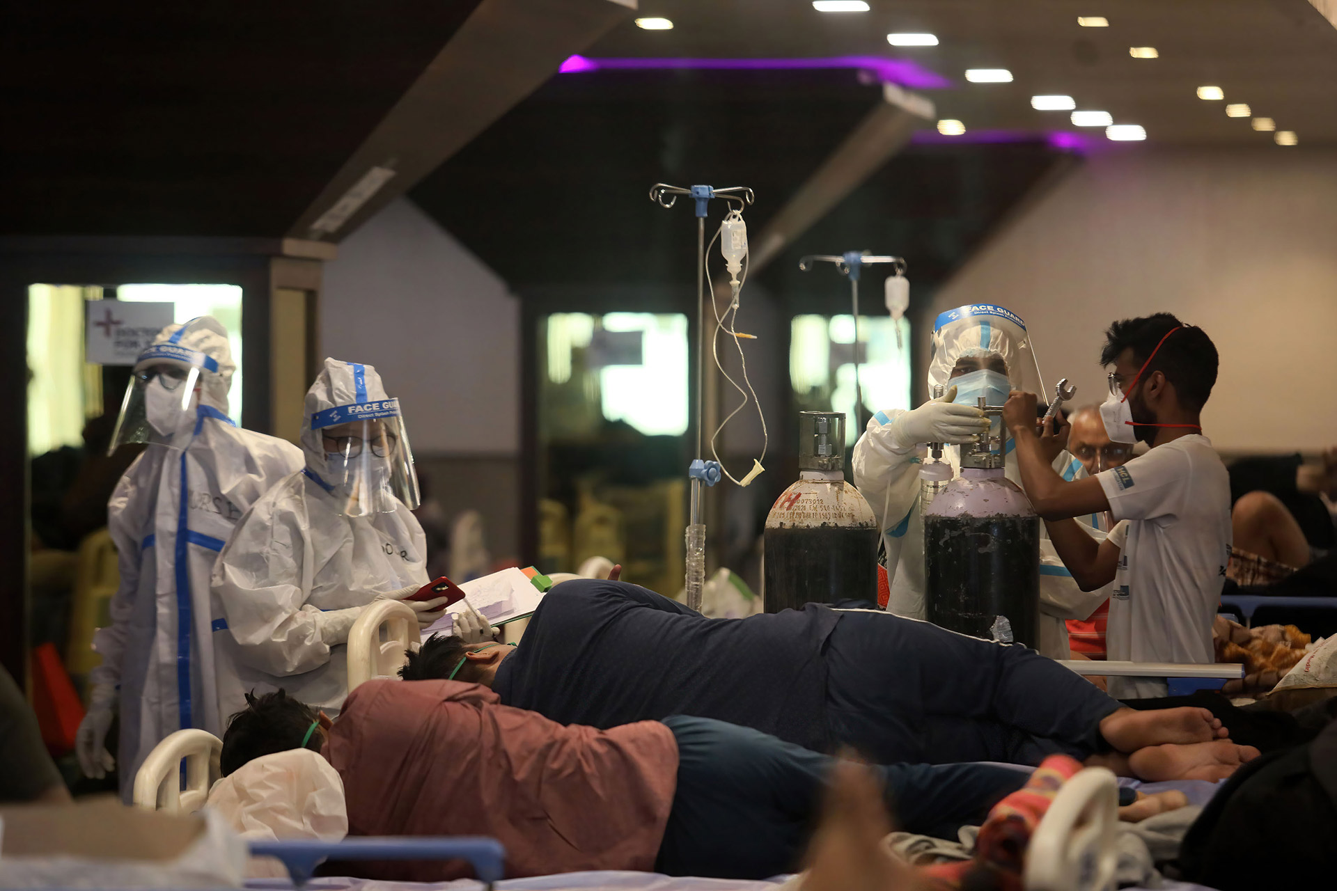 Drei Menschen in Schutzausrüstung kümmern sich um Menschen auf Krankenhaus-Liegen.