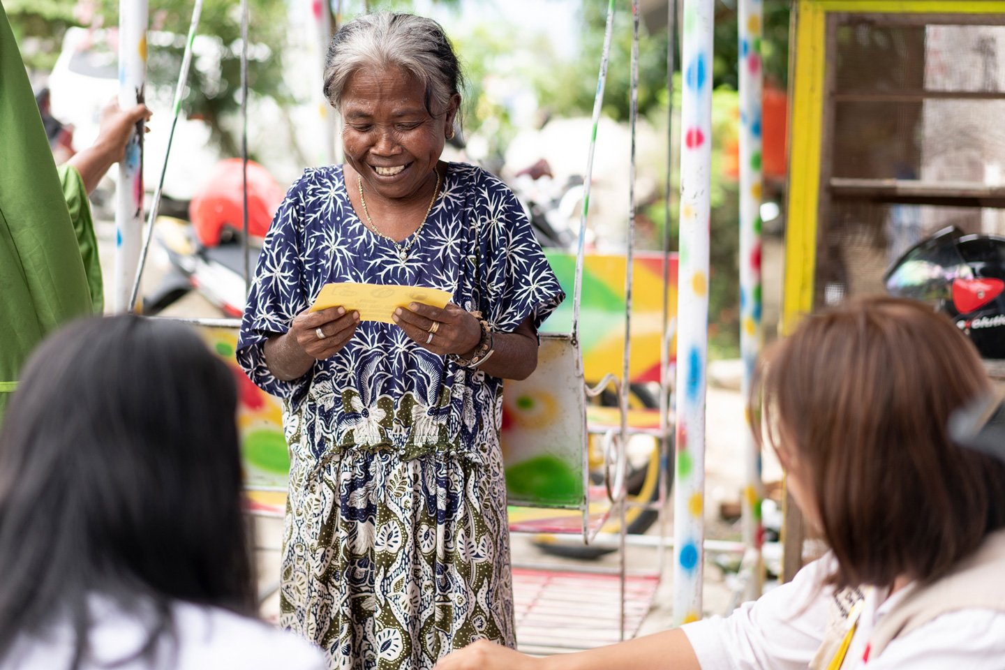 Eine ältere Frau hält einen gelben Zettel in der Hand, schaut auf ihn und lächelt.