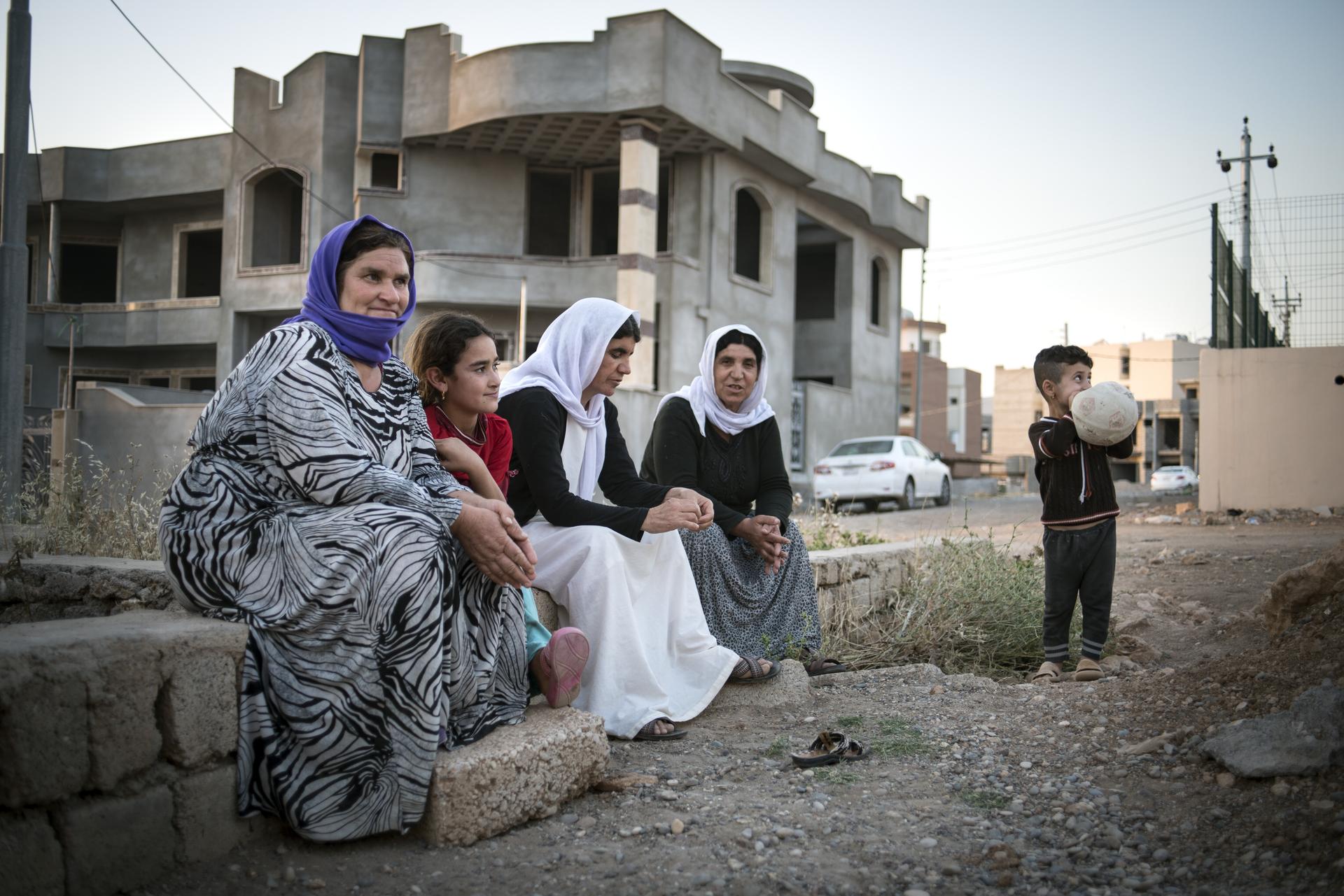 Eine Gruppe jesidischer Flüchtlinge sitzt innerhalb einer Siedlung von Hausrohbauten