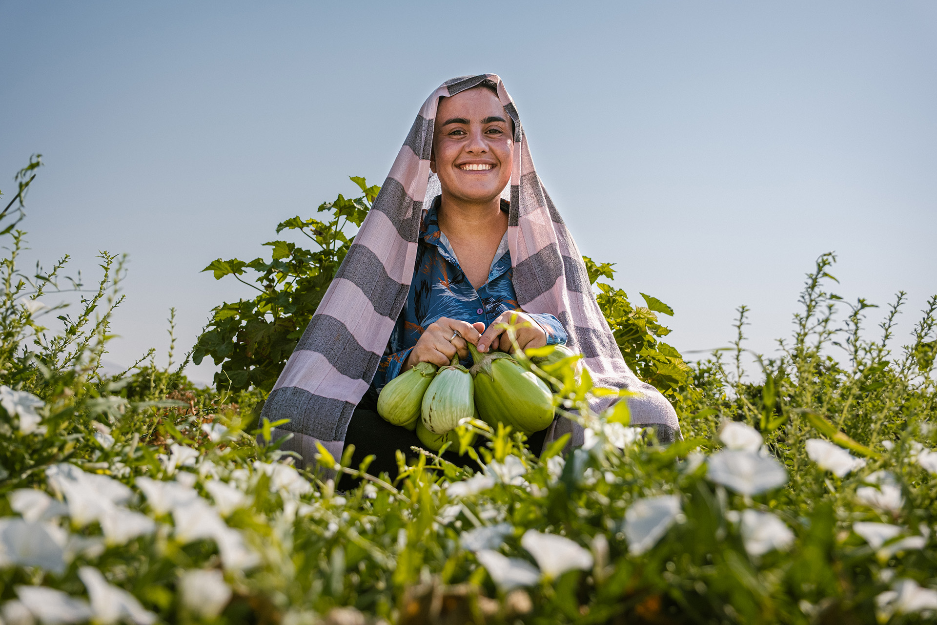 Frau sitzt in einem Feld und hält Obst in der Hand.