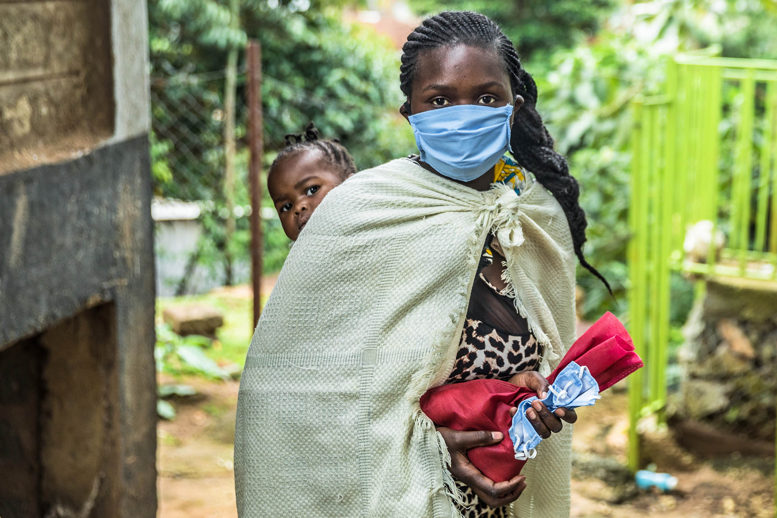 Eine Frau mit Mundschutz und einem Kind auf dem Rücken.