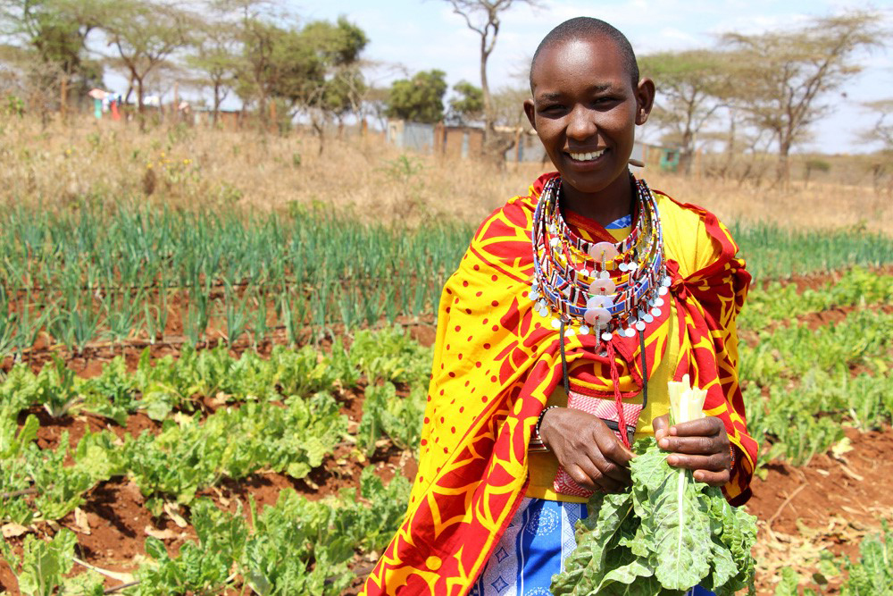 Eine Frau steht mit ihrer Ernte auf dem Feld, Kenia 2020. 